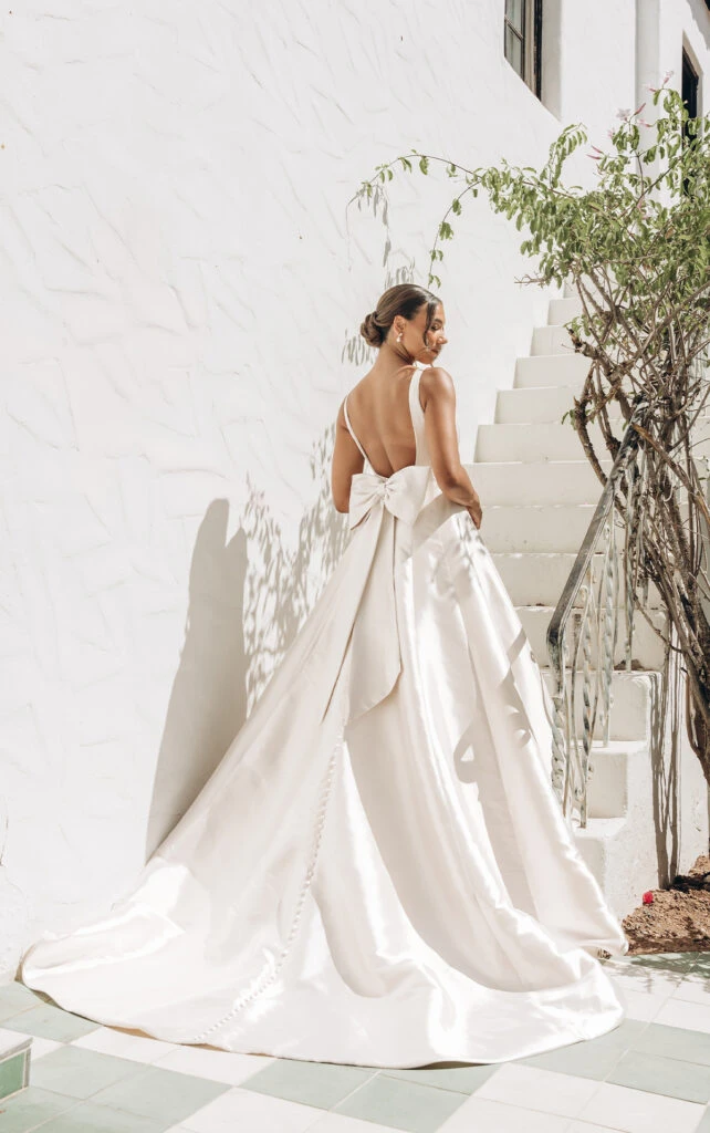 Bride wearing simple wedding dress with open back and bow accent.