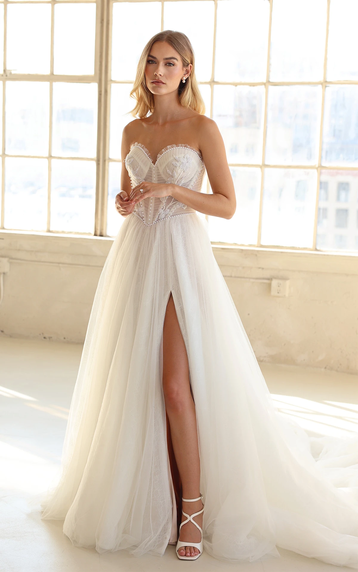 Bride wearing strapless tulle wedding dress in front of window.