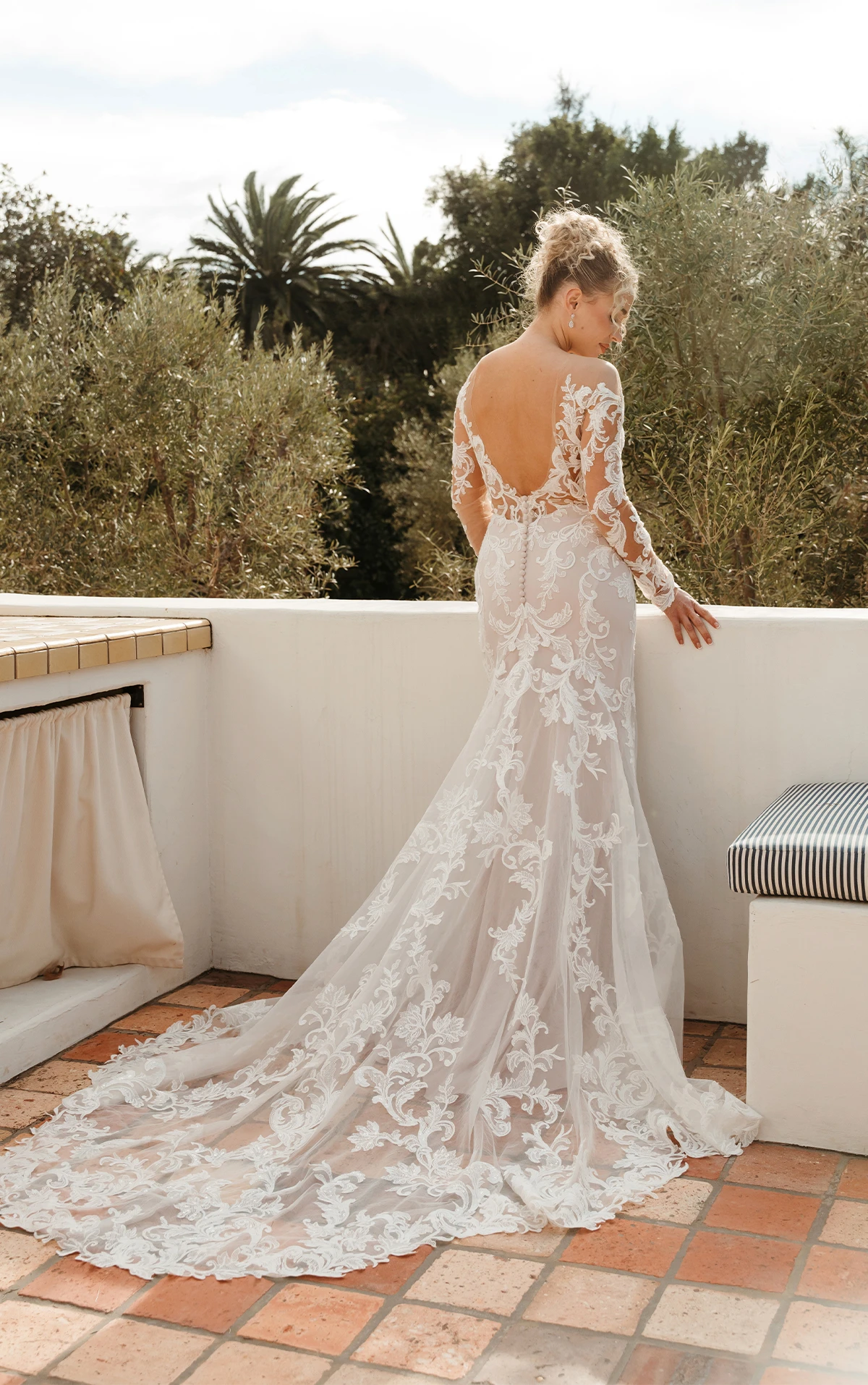 Bride wearing open back wedding dress with long sleeves and lace on balcony