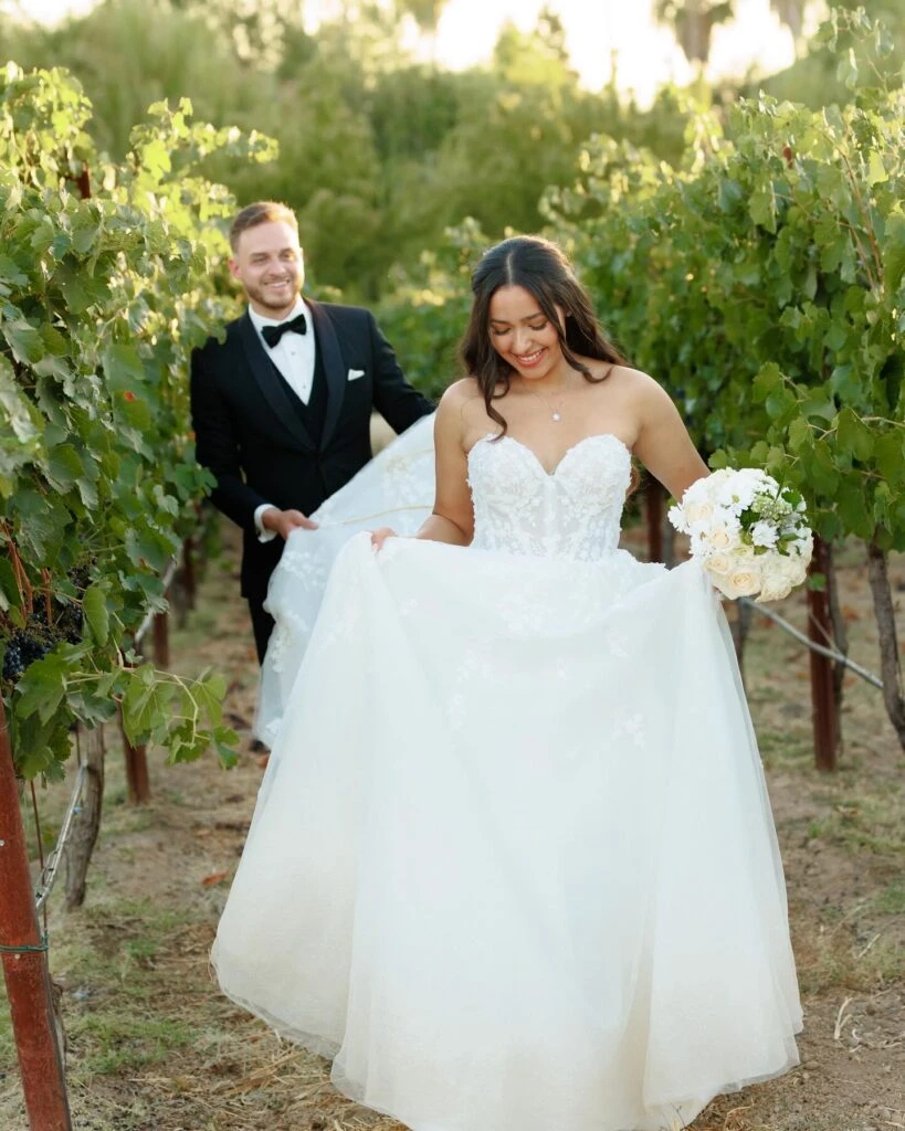 real bride mailin holding wedding dress walking in front of husband - Style 1483 by Martina Liana