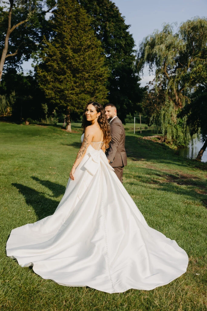 real bride olivia posed with husband looking over shoulder in grassy field - style 7711 by Stella York