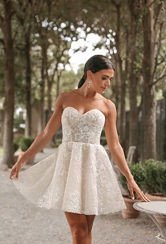 bride holding out skirt of her short wedding dress while looking down at table - D4133 by Essense of Australia