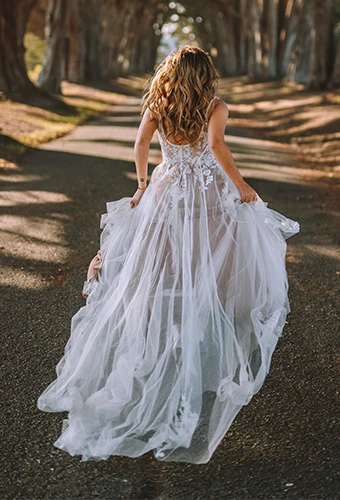 Bride wearing boho lace wedding dress with underlayer running in the woods