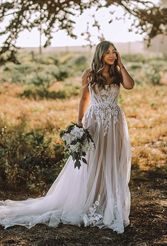 Bride wearing boho floral lace wedding dress with underlayer holding flower bouquet