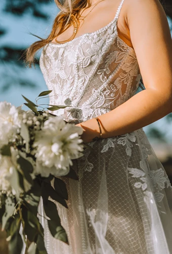Close up of bride wearing boho lace wedding dress with square neckline holding flower bouquet