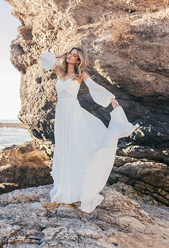 model standing on rocks by the ocean wearing all who wander's remi gown