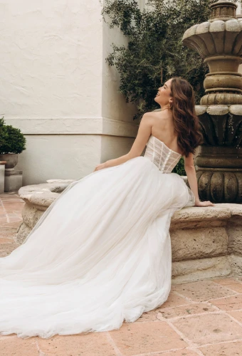 Bride wearing strapless wedding dress sitting on fountain