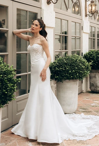 Bride wearing strapless lace wedding dress in front of window