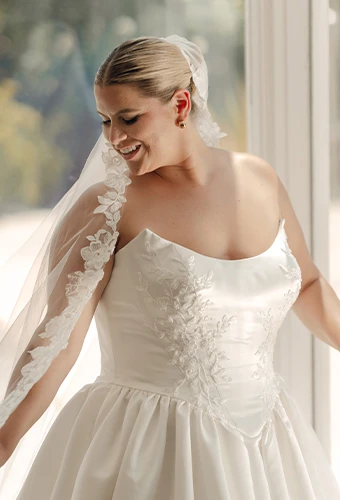 Plus size bride wearing strapless wedding dress with scoop neckline and lace details
