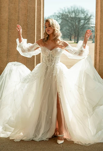 Bride wearing boho lace and tulle wedding dress with blouson off-the-shoulder sleeves and high leg slit