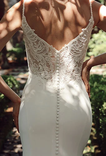 Bride wearing fit-and-flare wedding dress with lace details and v-back with fabric-covered buttons