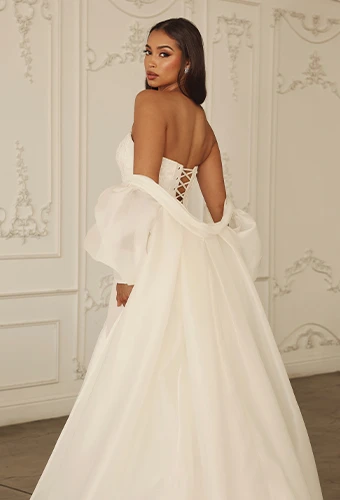 Bride wearing strapless satin wedding dress with lace up back detail and detachable overskirt