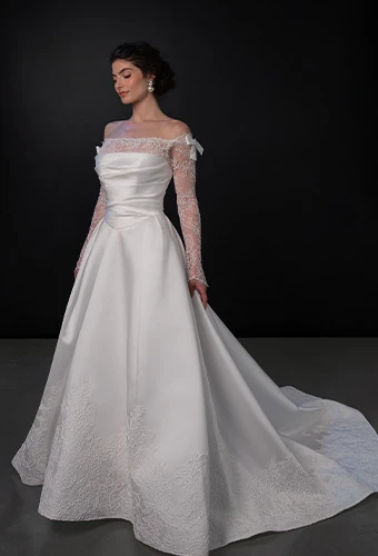 Bride wearing satin wedding dress with lace off-the-shoulder long sleeves and bow details