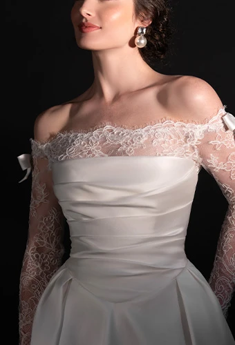 Bride wearing satin wedding dress with lace off-the-shoulder long sleeves and bow details and straight across neckline