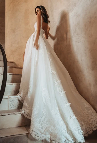Bride in a classic white wedding gown with architectural open back and beaded lace train detail, photographed from behind on stone steps