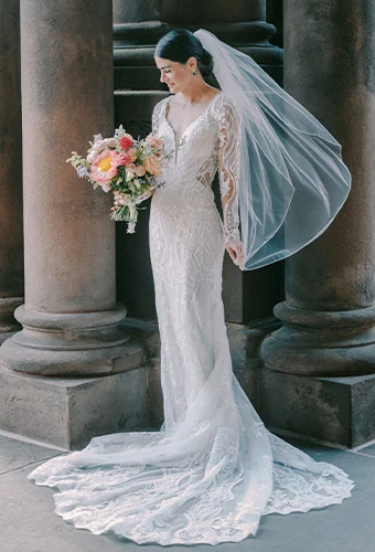 Bride posed in front of columns holding a vibrant bouquet wearing Essense of Australia D3150.