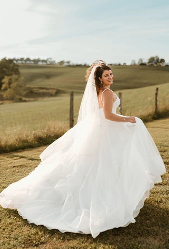 Bride running in an open field in voluminous wedding gown , Stella York SY7817.