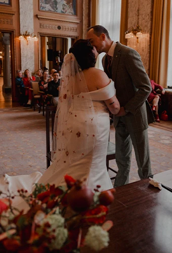 Real bride Priscilla and groom Vincent share a sweet moment during their indoor wedding ceremony surrounded by guests.