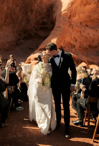 Newlyweds Erica and Trey sharing a kiss as they walk down the aisle past guests at their outdoor desert wedding.