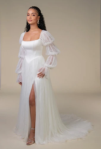 Bride wearing a white wedding dress with a fitted square-neckline bodice and high slit, styled with detachable pleated puff sleeves, photographed against a neutral background