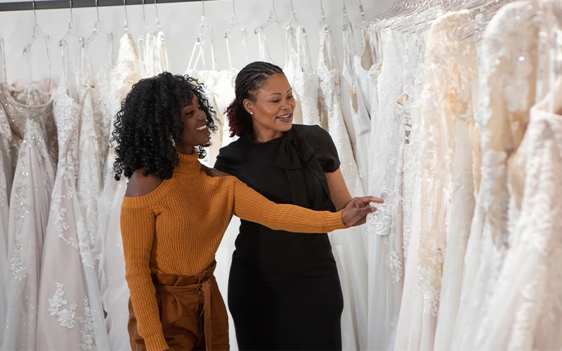 Bride and bridal stylist walk along wedding dress selection together.