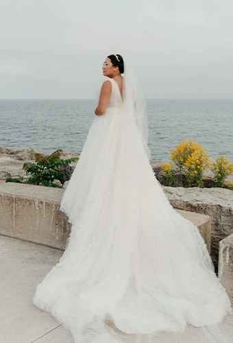 Real bride Lara in a white sleeveless wedding dress with flowing train, photographed overlooking the ocean