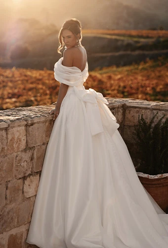 Bride wearing a-line wedding dress with asymmetrical one shoulder and floral accent and bow back detail