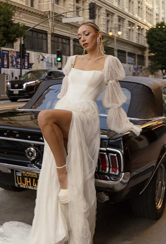 Bride wearing a line wedding dress with high leg slit and statement sleeves leaning on vintage car
