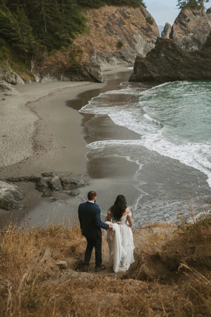 Real Bride Teresa and Eric walking down a cliff path toward the beach along the Oregon coast.