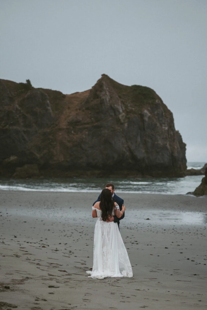 Real Bride Teresa and Eric embracing each other on a sandy Oregon coast beach.