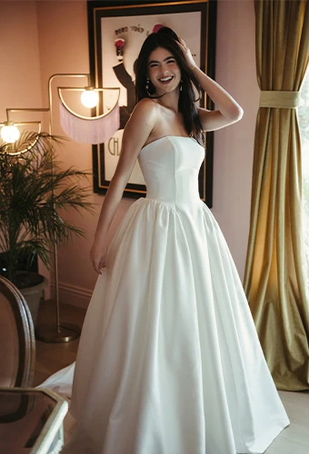 Bride wearing strapless ballgown with straight across neckline posing in a pink room