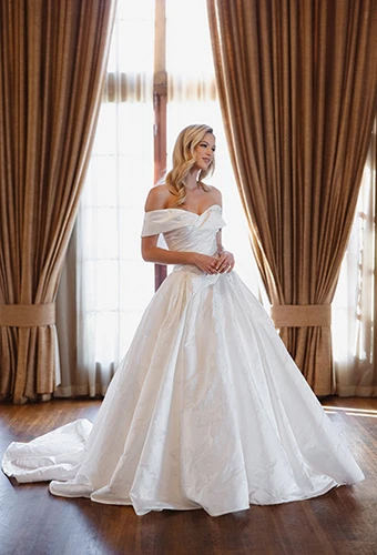Bride wearing off-shoulder ballgown wedding dress with defined bodice and basque waistline, Essense of Australia D4604