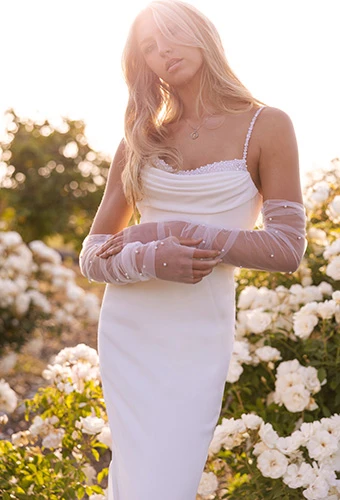 Bride poses in simple wedding dress with pearl straps, detailing, and sheer bridal gloves, Stella York SY7831