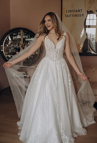 Bride smiling in an A-line wedding dress with plunging neckline, floral embellishments and cathedral veil, Stella York sy8314