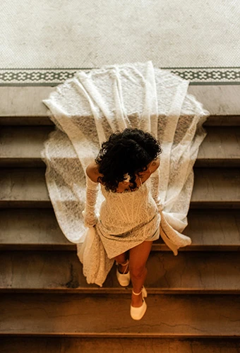 Bride walking down stairs with sheer lace train flowing behind her, All Who Wander hadley