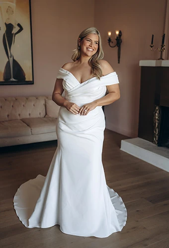 Bride smiles in plus-size fit-and-flare wedding dress with off shoulder straps, Stella York SY8330+