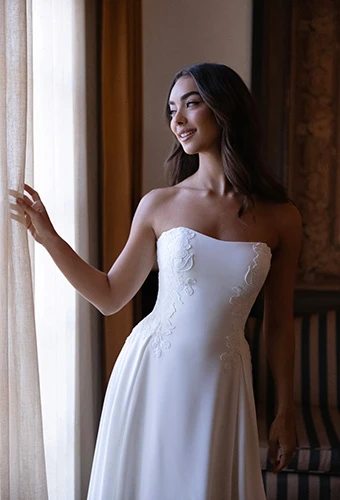 Bride looking out the window in a strapless crepe gown with minimal floral details, Essense of Australia D4504