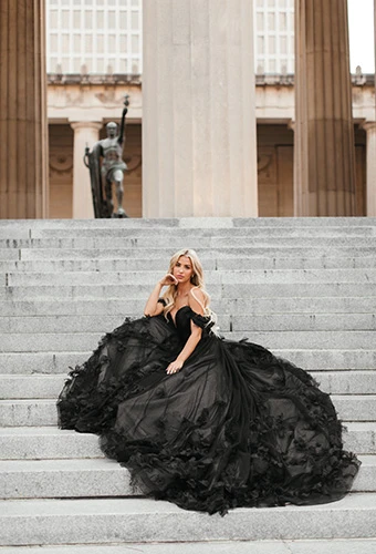 Bride sitting on steps wearing voluminous black wedding ballgown with delicately placed 3D florals, Essense of Australia D3734BLK
