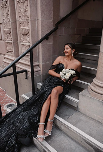 Bride sitting wearing black shimmering A-line wedding dress with high slit, Essense of Australia D3648BLK
