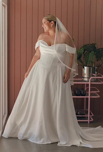 Plus size bride wearing A-line wedding dress with corset boning and off-shoulder straps with tulle veil, Stella York SY8236+