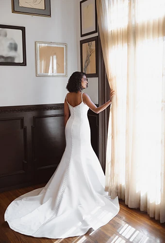 Bride wearing fit-and-flare wedding dress with spaghetti straps and a zipper closure finished with fabric buttons, Essense of Australia D4609