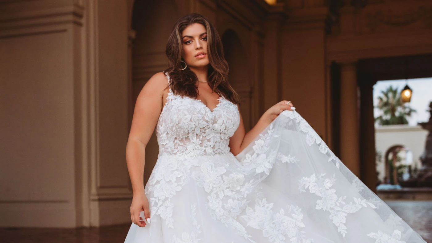 A plus-size with brown hair in a lacy white wedding dress with thin straps.