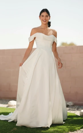 Stella York SY8236 A-Line wedding dress with a strapless sweetheart neckline, lace bodice, and airy tulle skirt. Model poses outdoors on grass with a soft pink wall and trees in the background.