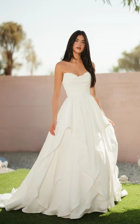Ballgown wedding dress by Stella York, style SY8212. Features a strapless sweetheart neckline, floral lace bodice, and a full tulle skirt. Photographed outdoors on grass with a pink wall and trees.