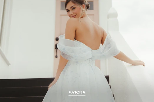 Stella York bridal gown SY8215, a light and airy off-the-shoulder A-line dress with a subtle blue floral pattern and full tulle skirt, shown from the back as the bride smiles.