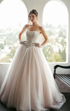 Bride wearing SY8189, a ballgown dress while standing next to a bench in front of arch windows.